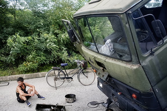 A man sits near a broken down truck being repaired on the highway outside Pyongyang, North Korea